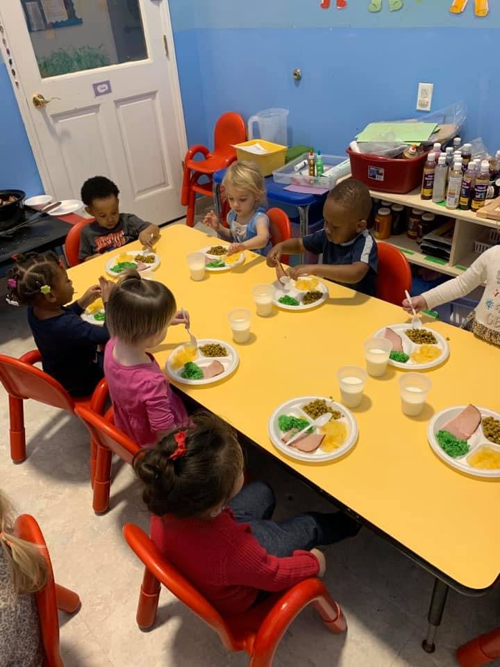 Children sitting at a yellow table eating a meal