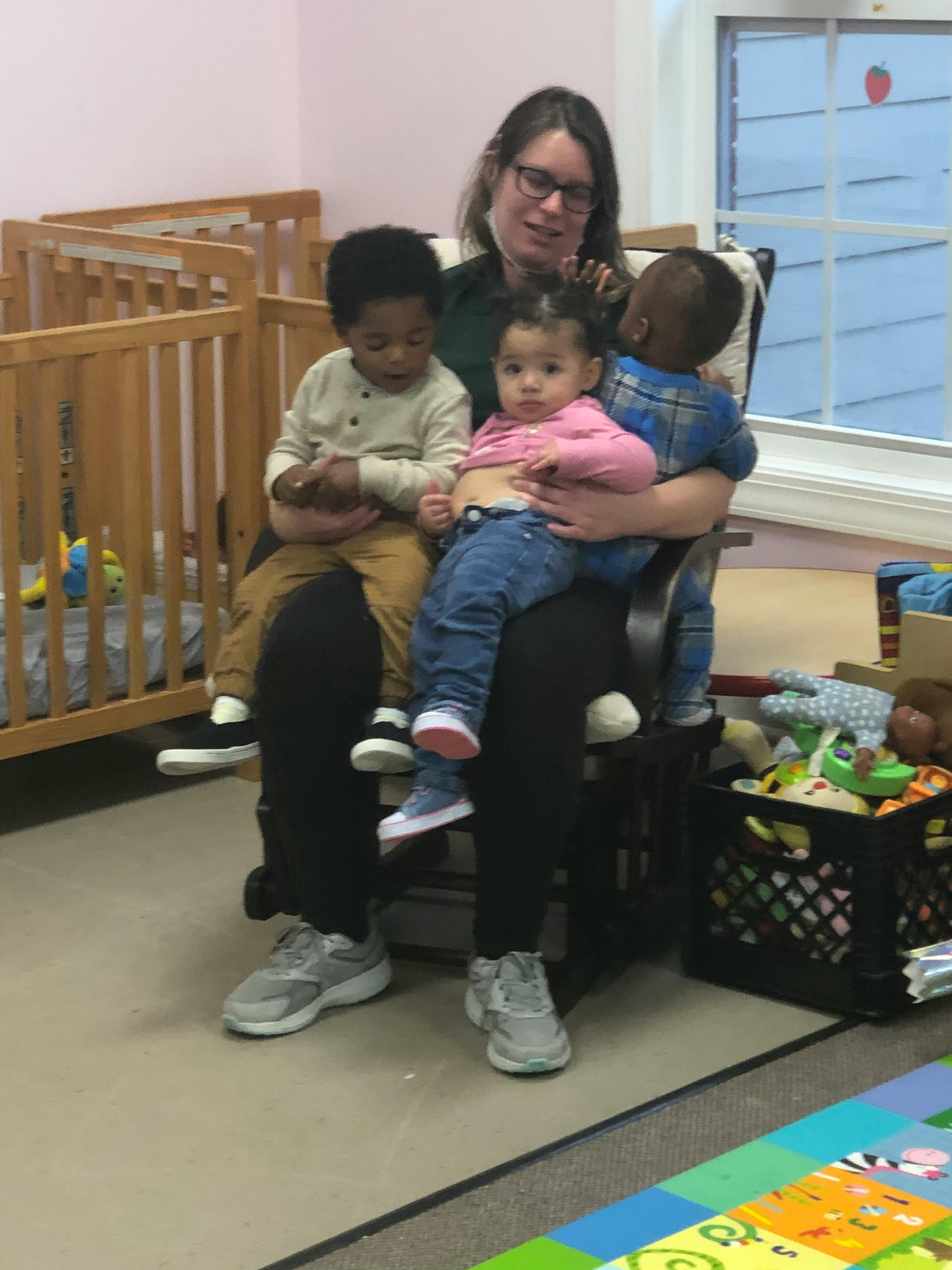 Person sitting in a chair holding two children, with another child next to them