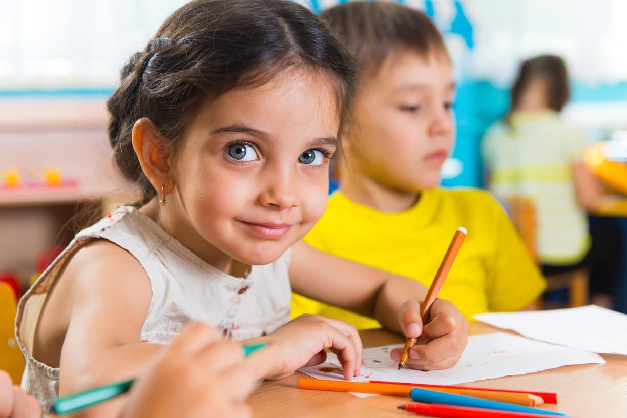 Child drawing with colored pencils at a table in a classroom
