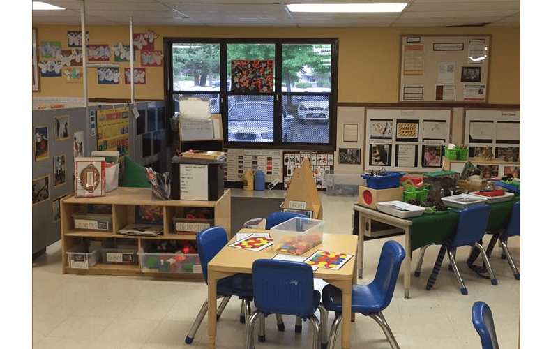 Classroom with small tables and chairs, shelves with toys, and posters on the walls