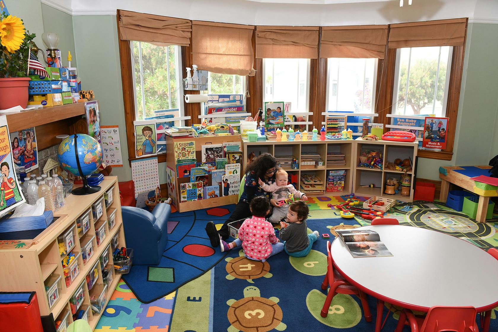 Adult and three children playing on a rug in a classroom
