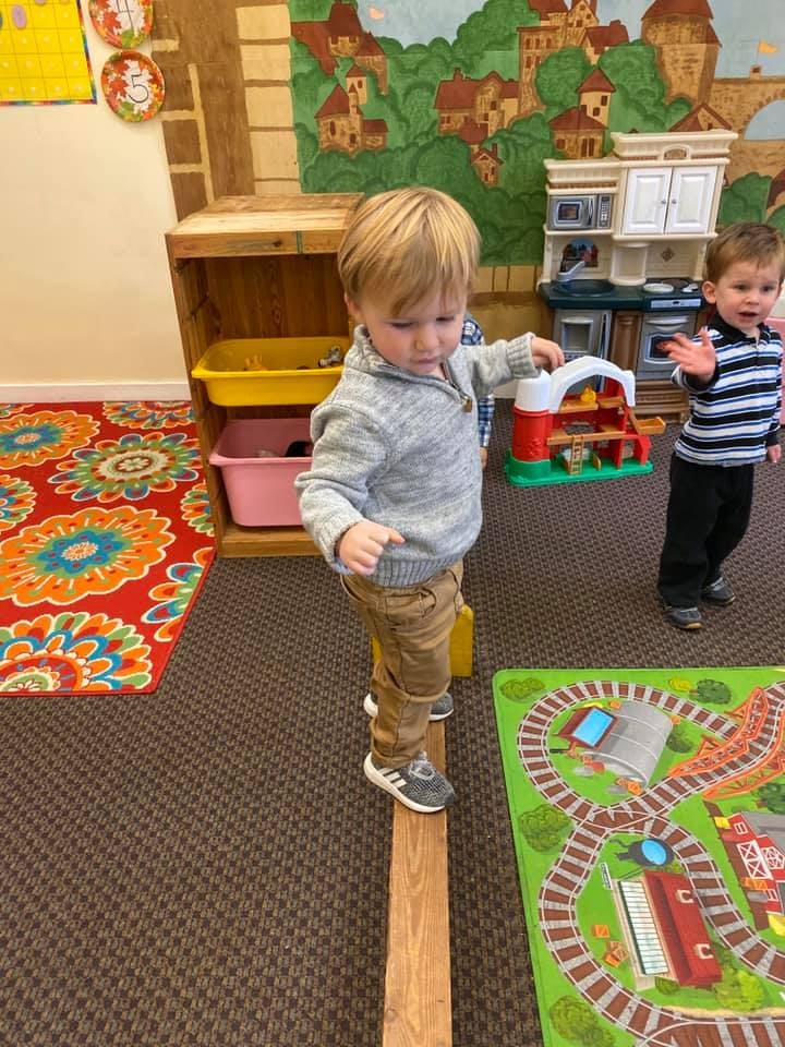 Child balancing on a wooden beam in a classroom