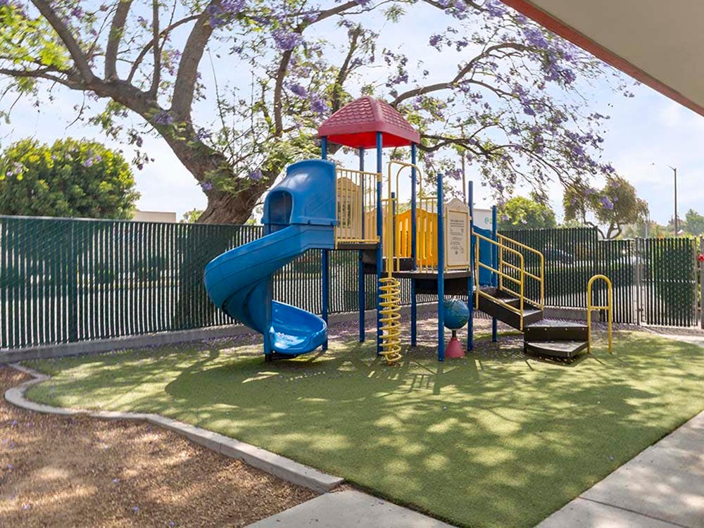 Playground with blue slide, yellow and red play structure, and artificial turf