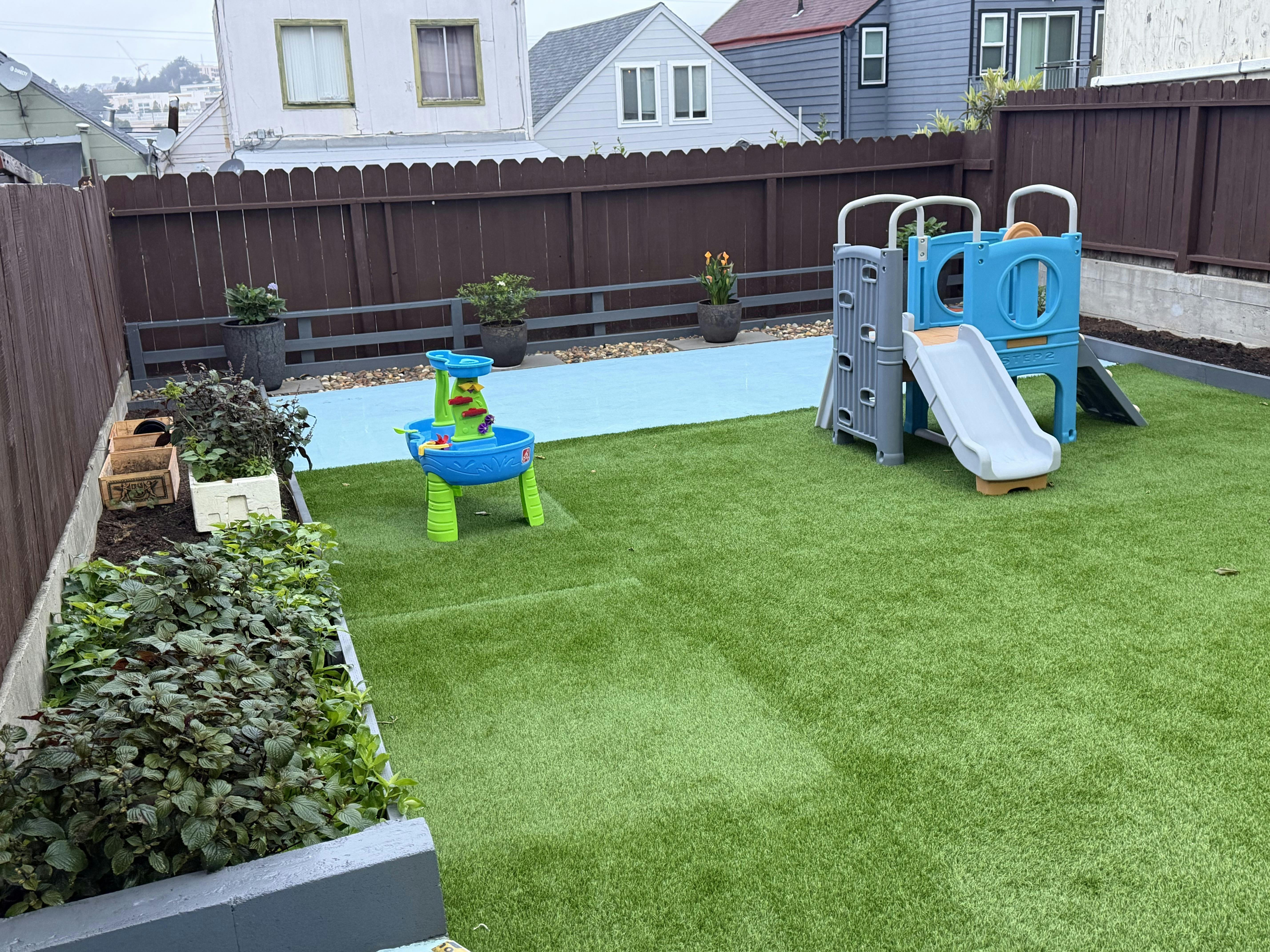 Backyard play area with a plastic slide and water table on artificial grass