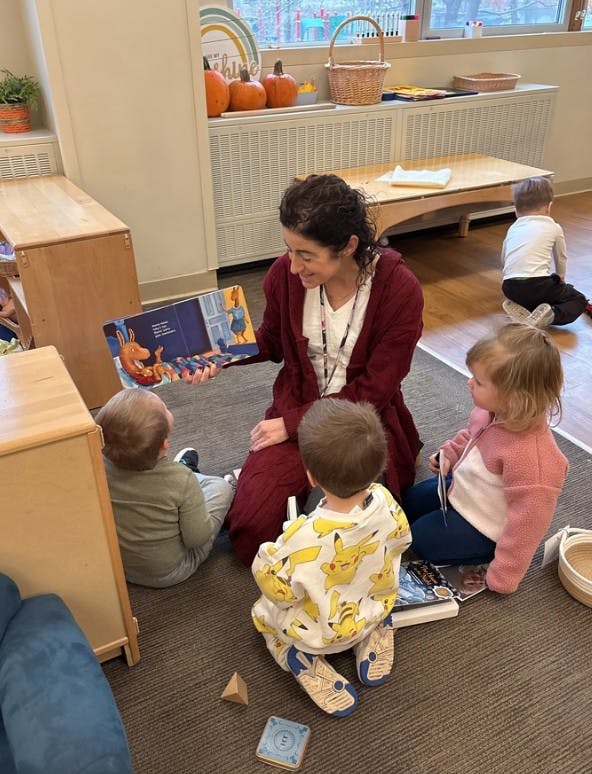 Adult reading a book to three children in a classroom