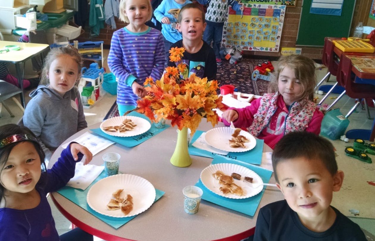 Children sitting around a table with plates of food and a floral centerpiece