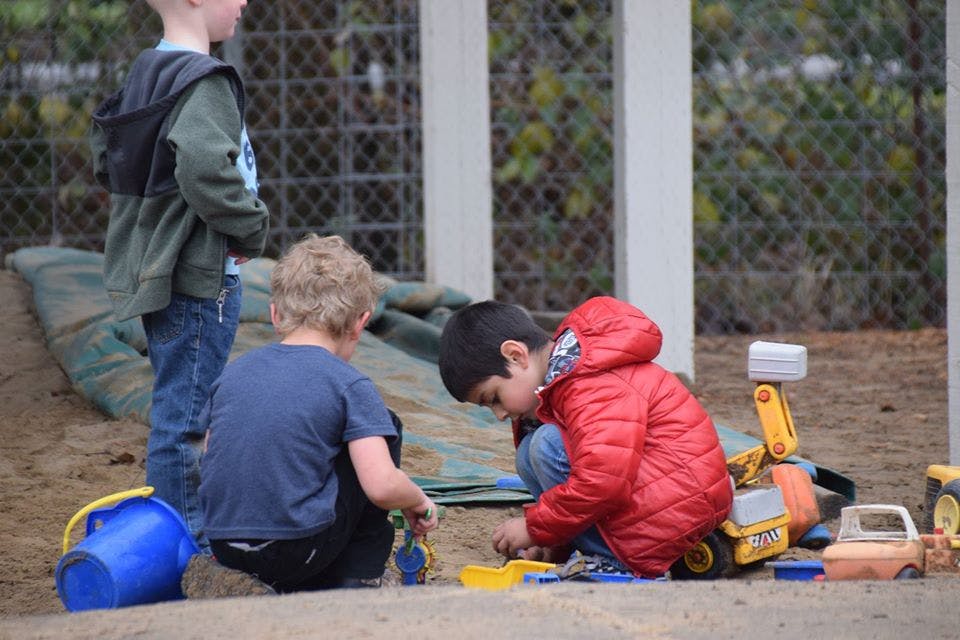 Three children playing in dirt with toys