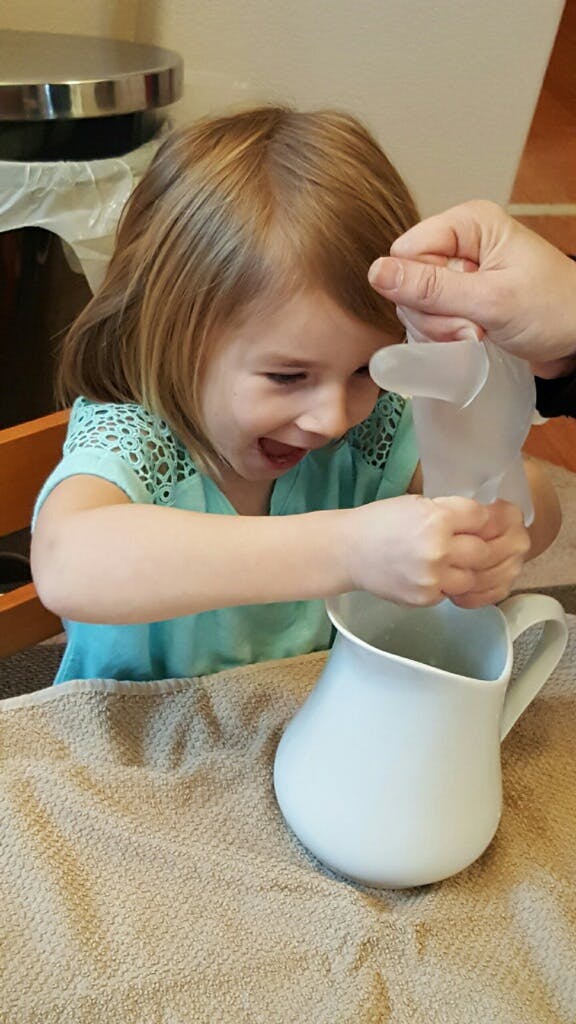 Child putting a clear glove into a white pitcher