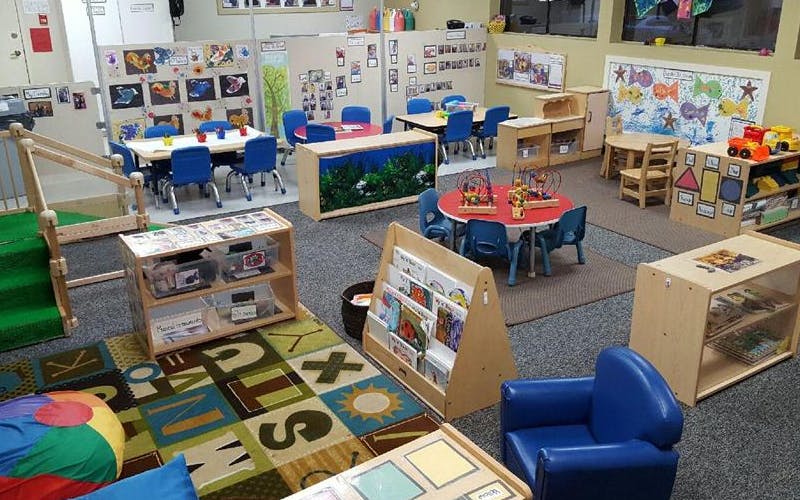 A colorful empty daycare classroom with small tables, chairs, and play areas