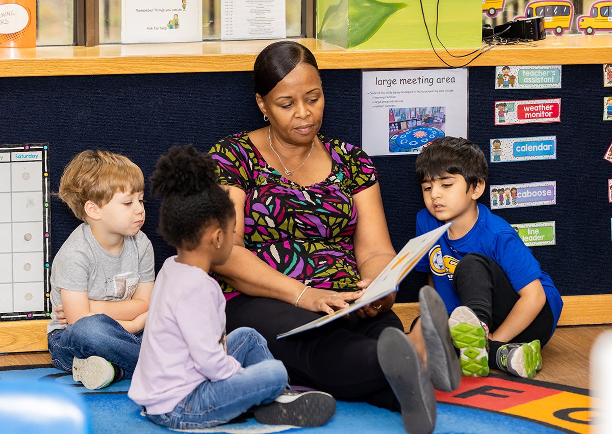 Person reading a book to three children in a classroom