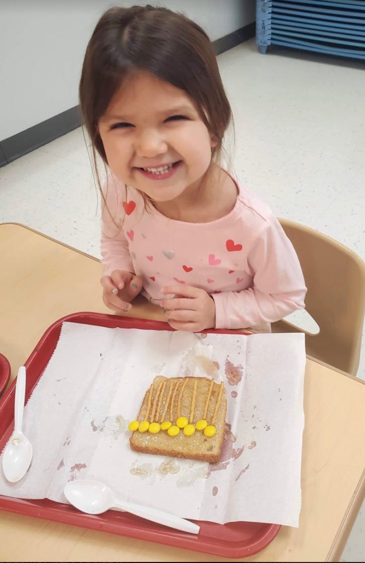 Child sitting at a table with a decorated piece of toast on a tray