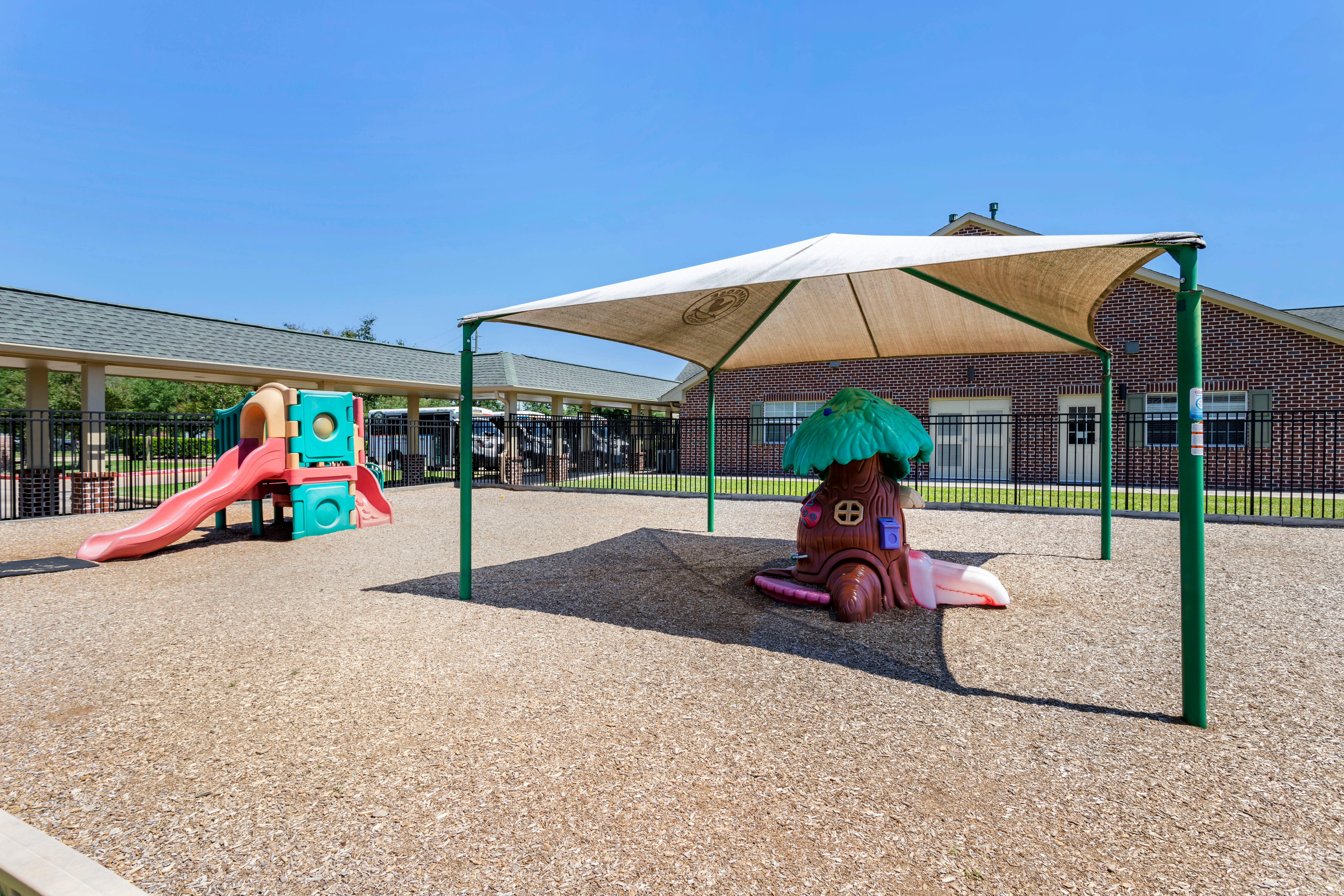 A colorful playground with slides and a tree-shaped play structure under a shade