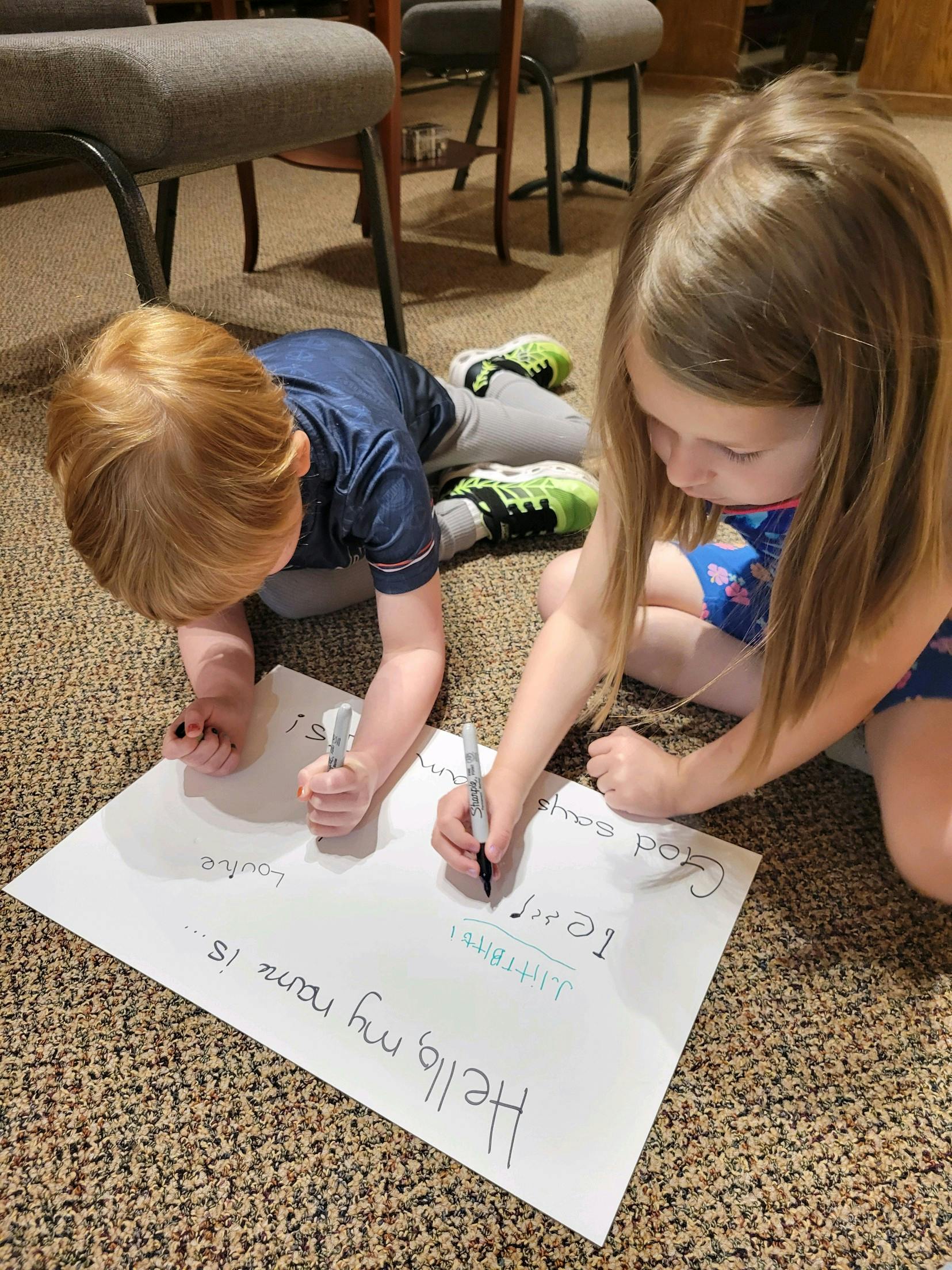 Two children writing on a large piece of paper on the floor