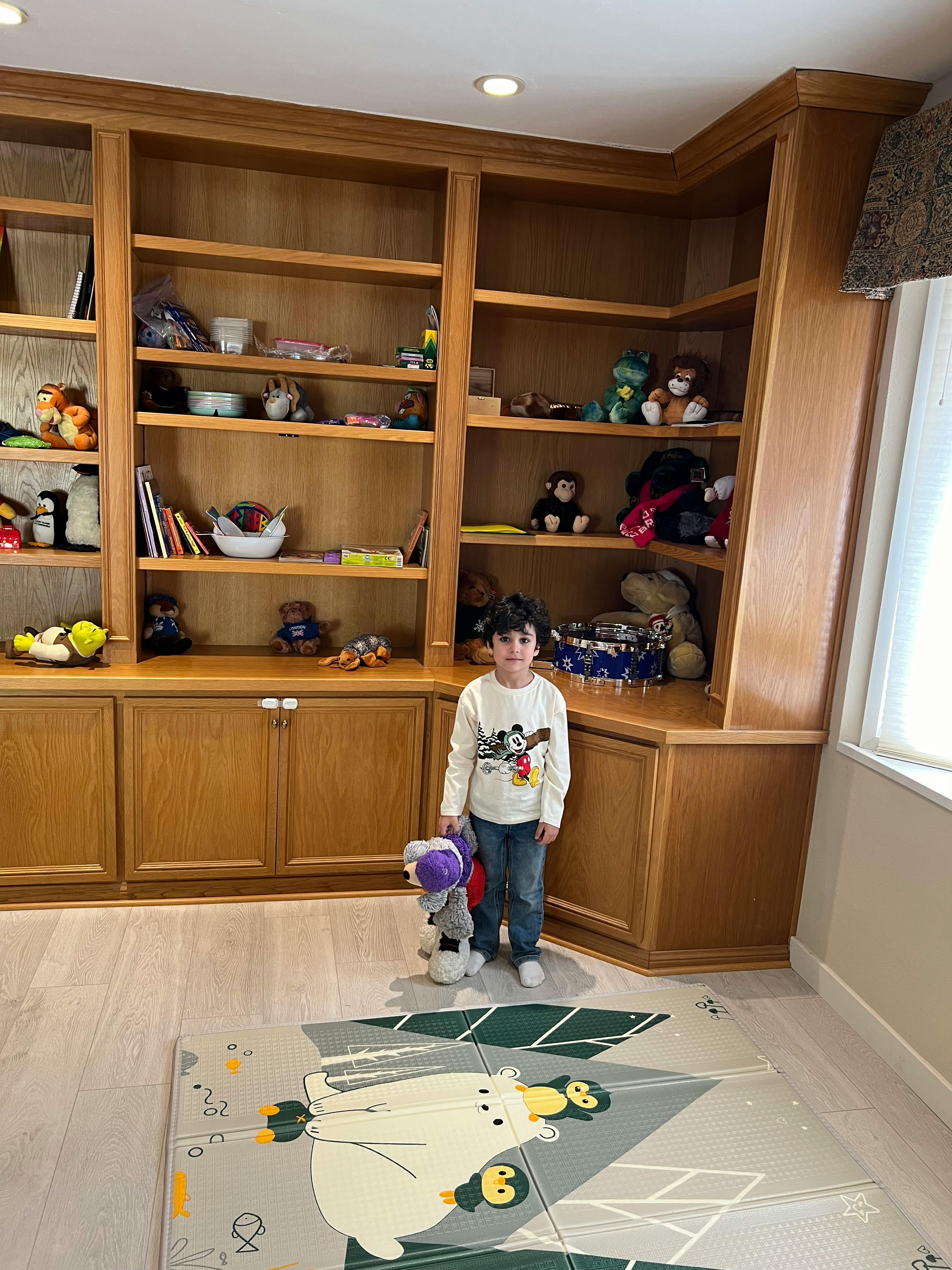 Child standing in front of a wooden bookshelf holding a stuffed animal