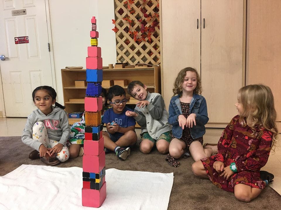 Children sitting around a tall tower of colorful blocks