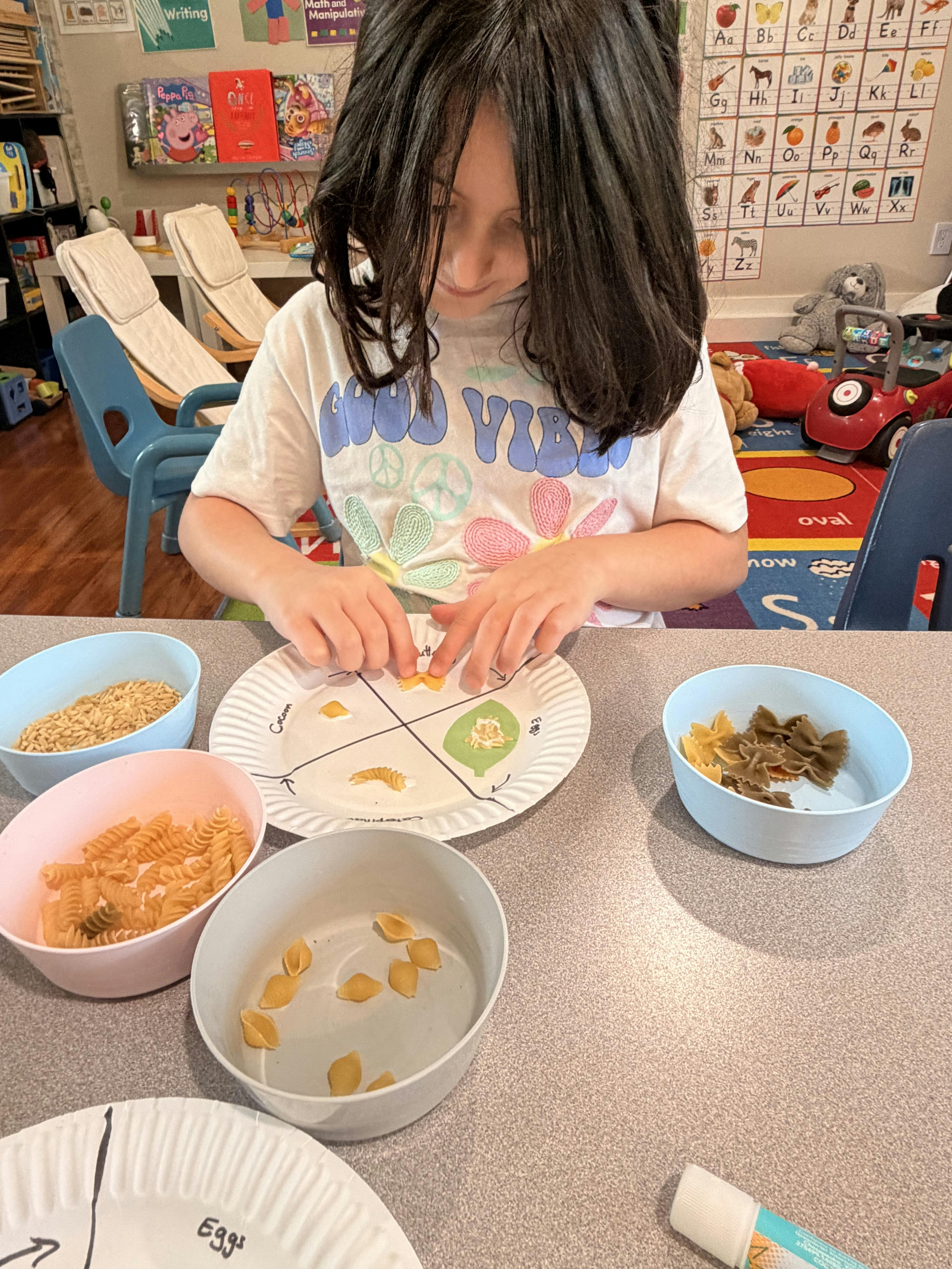 Child manipulating pasta shapes on a paper plate marked with a diagram in a classroom