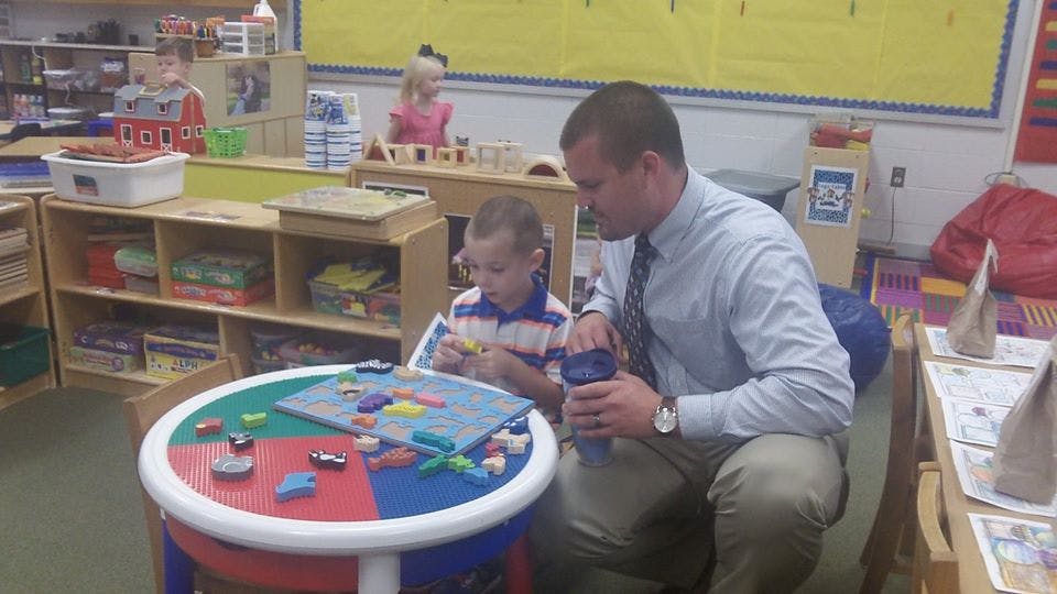 Adult and child playing with toys at a small table in a classroom