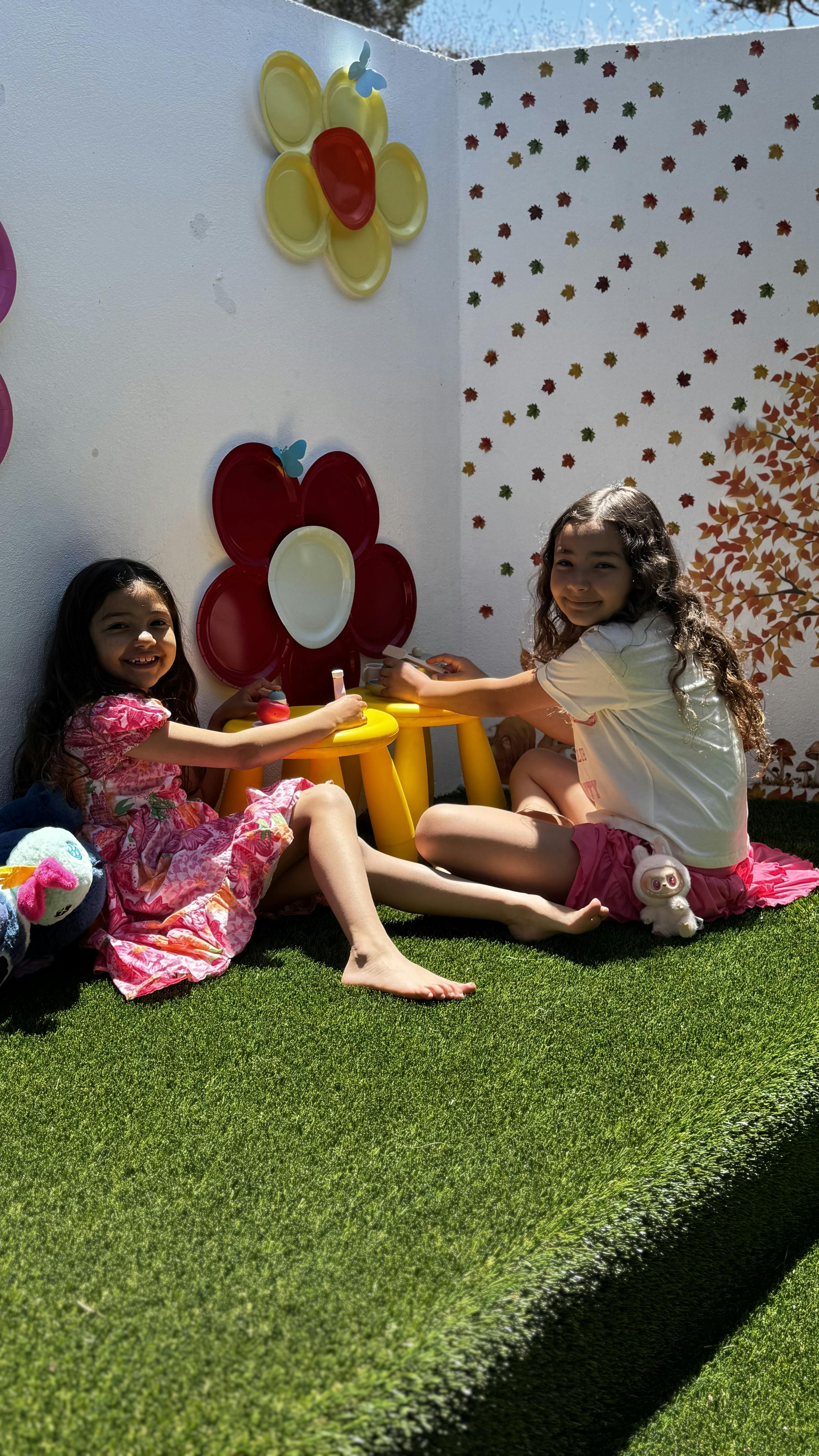 Two children sitting on artificial grass with a small yellow table