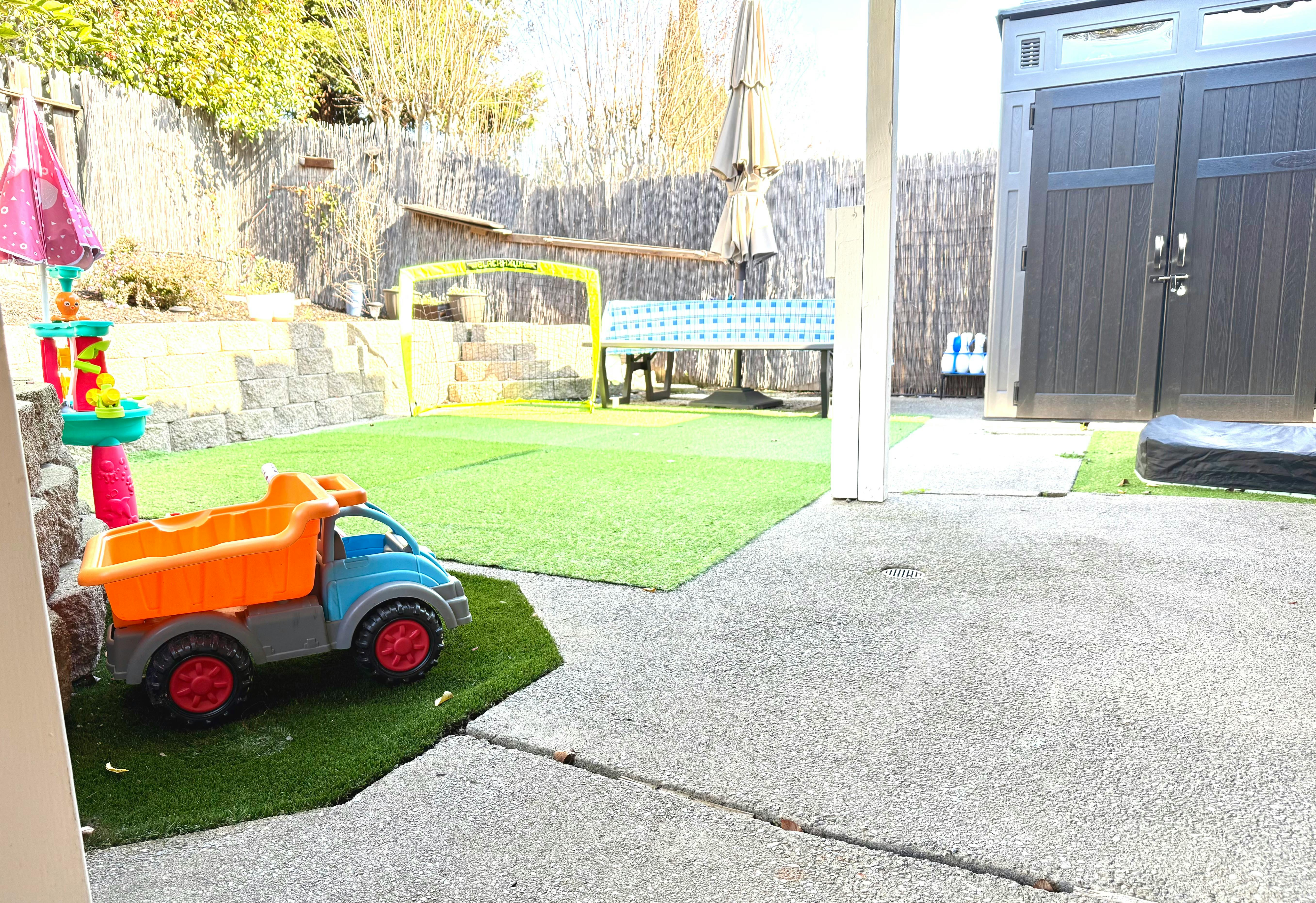Toy dump truck and other toys on artificial grass in a backyard