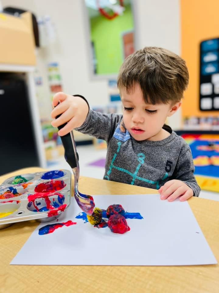 Child painting with a spoon and colorful paint on paper