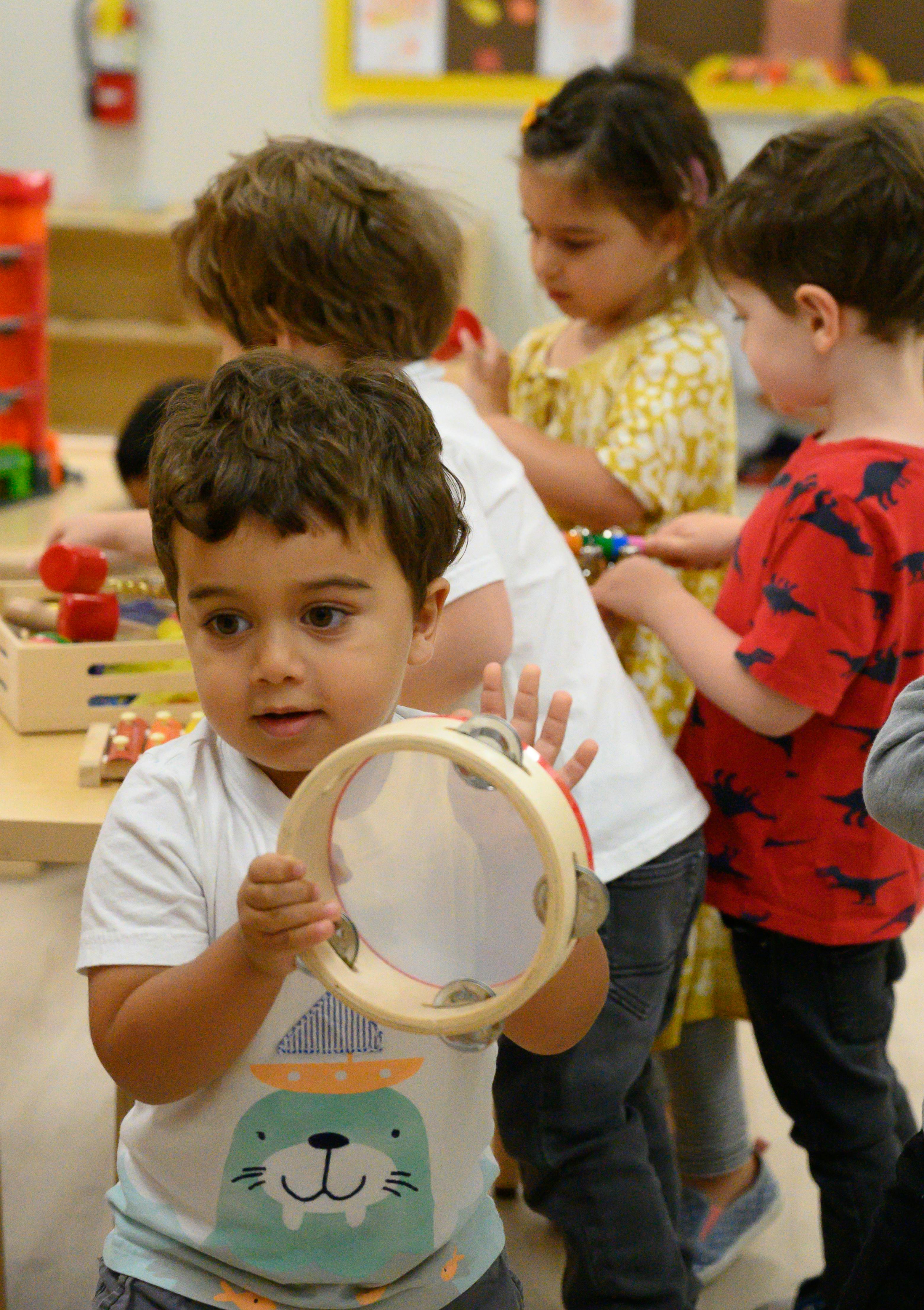 Child holding a tambourine in a classroom with other children
