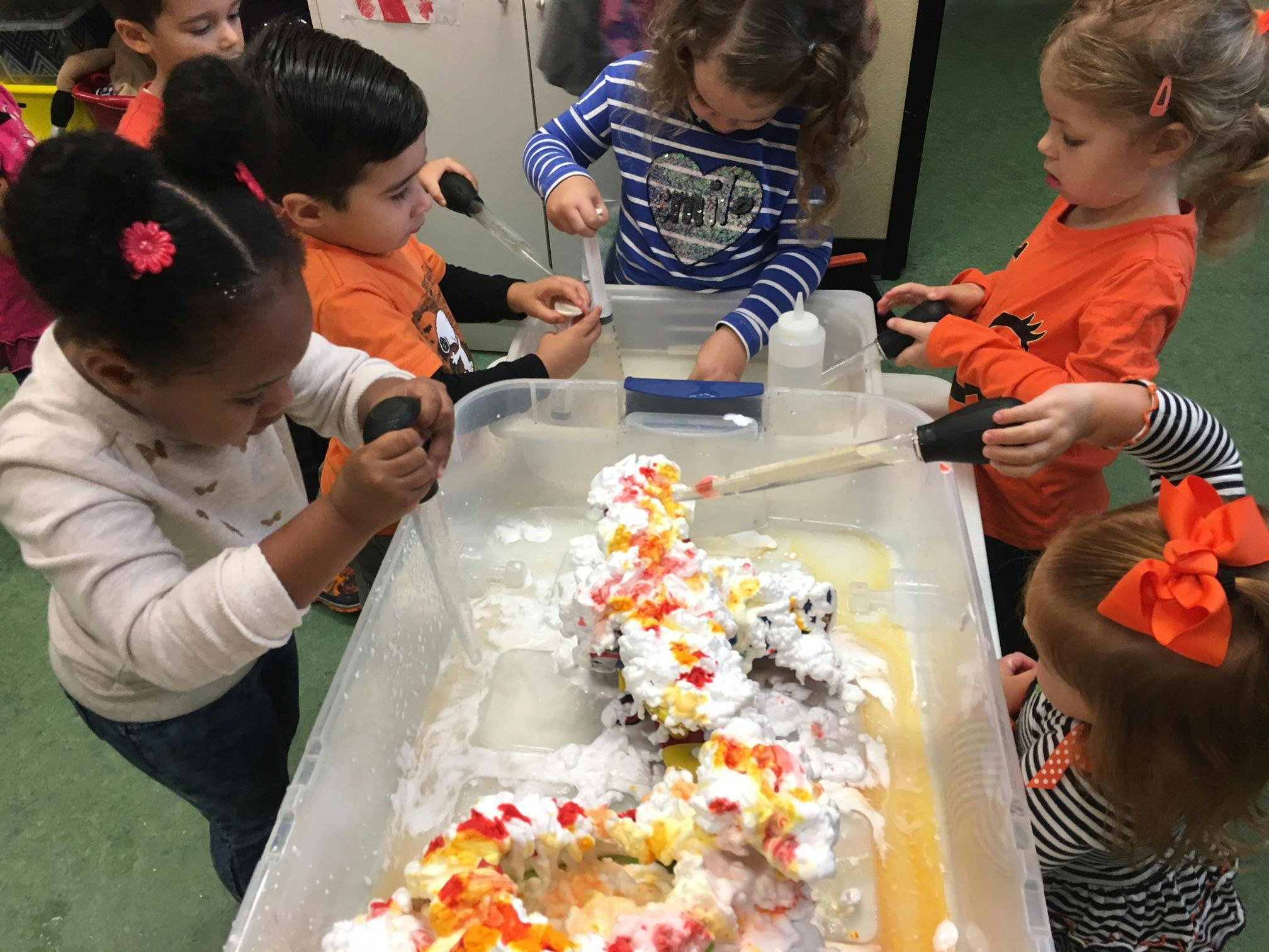 Children playing with shaving cream and colored liquid in a sensory bin