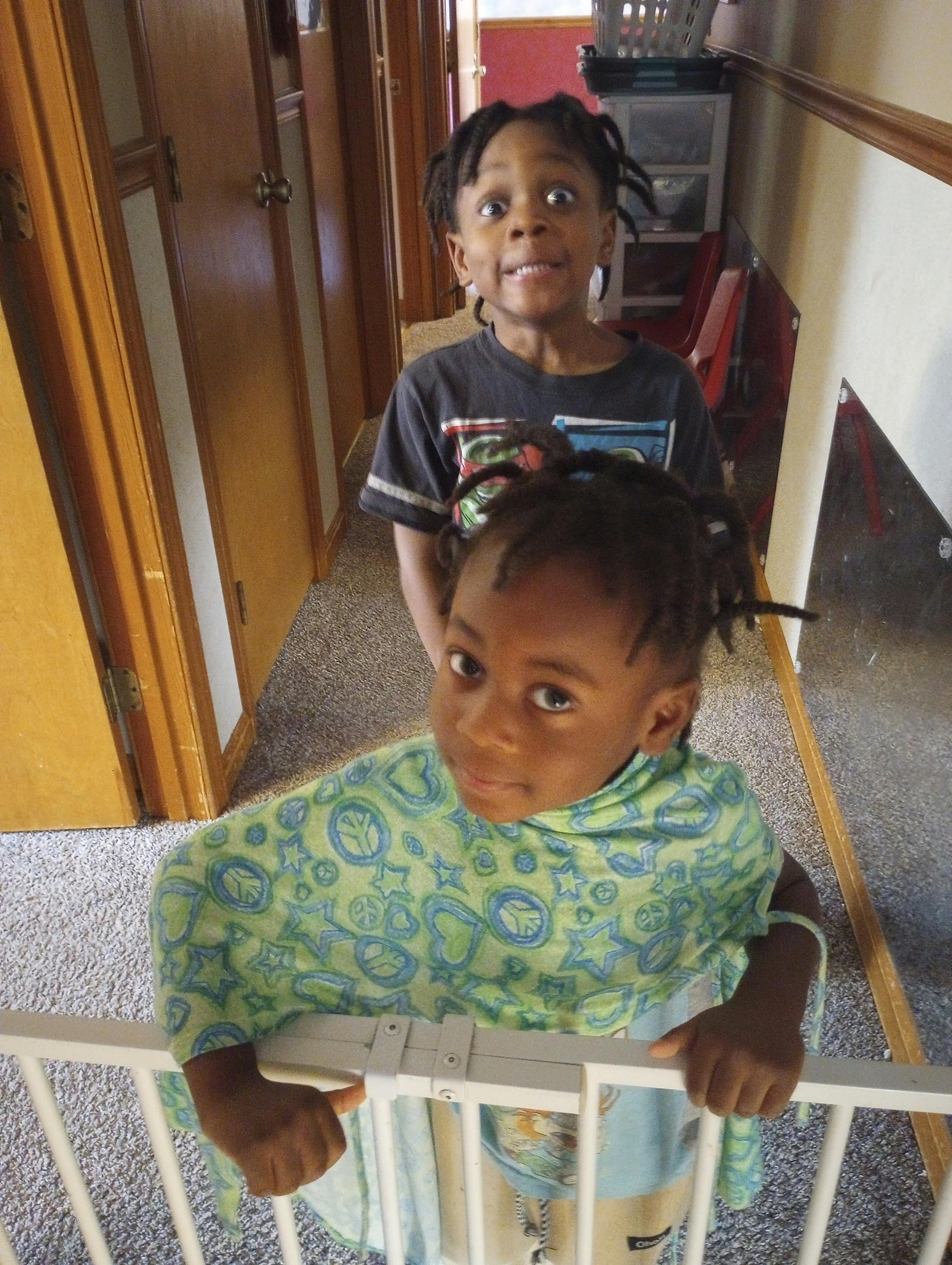 two children looking up at the camera, one wearing a green top and holding a rail