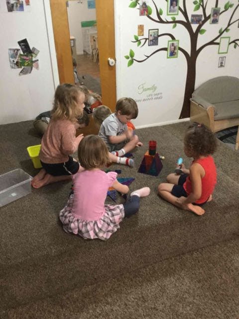 Four children sitting on a carpeted floor playing with toys