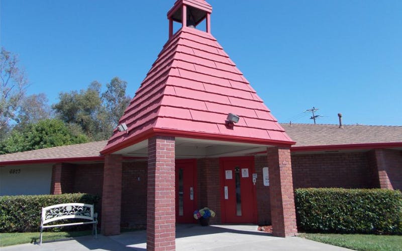 Brick building with a red roof and red double doors under a steeple