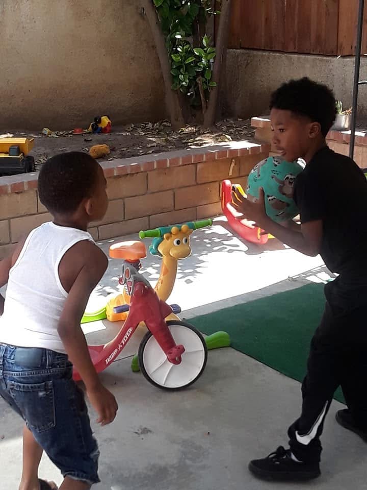 Two children playing with a ball in a backyard near a toy tricycle