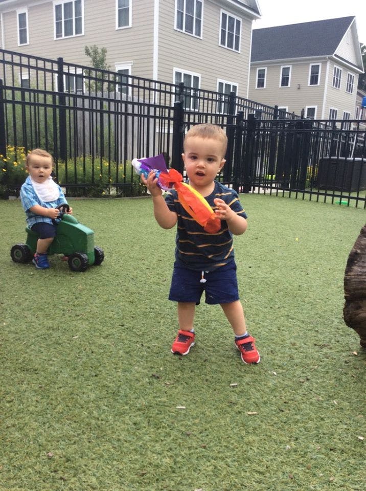 Two children playing outdoors, one holding a toy, another on a ride-on toy