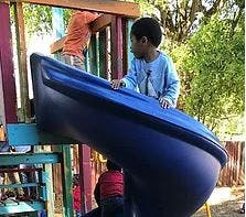 Child on top of a slide, another child climbing behind