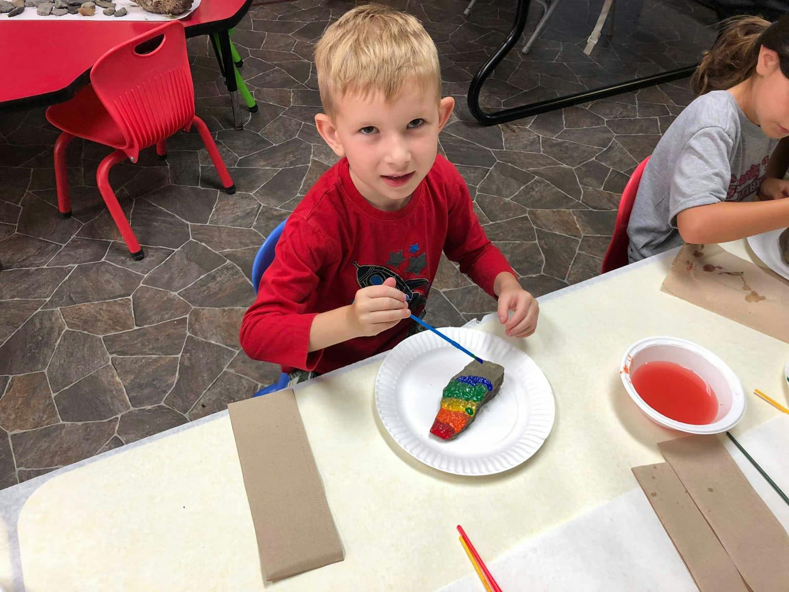 Child painting a rock with rainbow colors