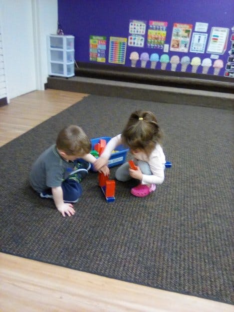 Two children playing with blocks on a carpeted floor