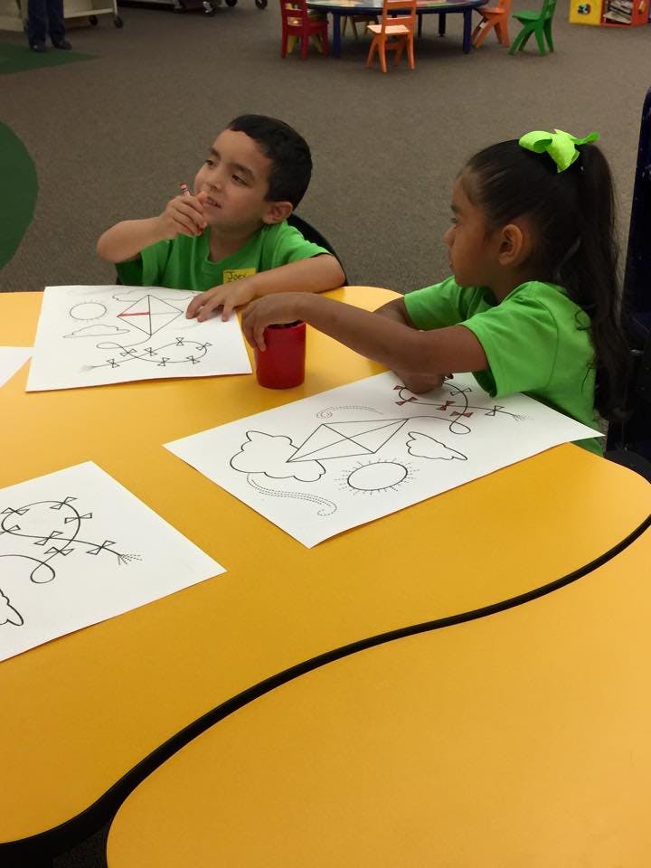 Two children at a yellow table with drawings