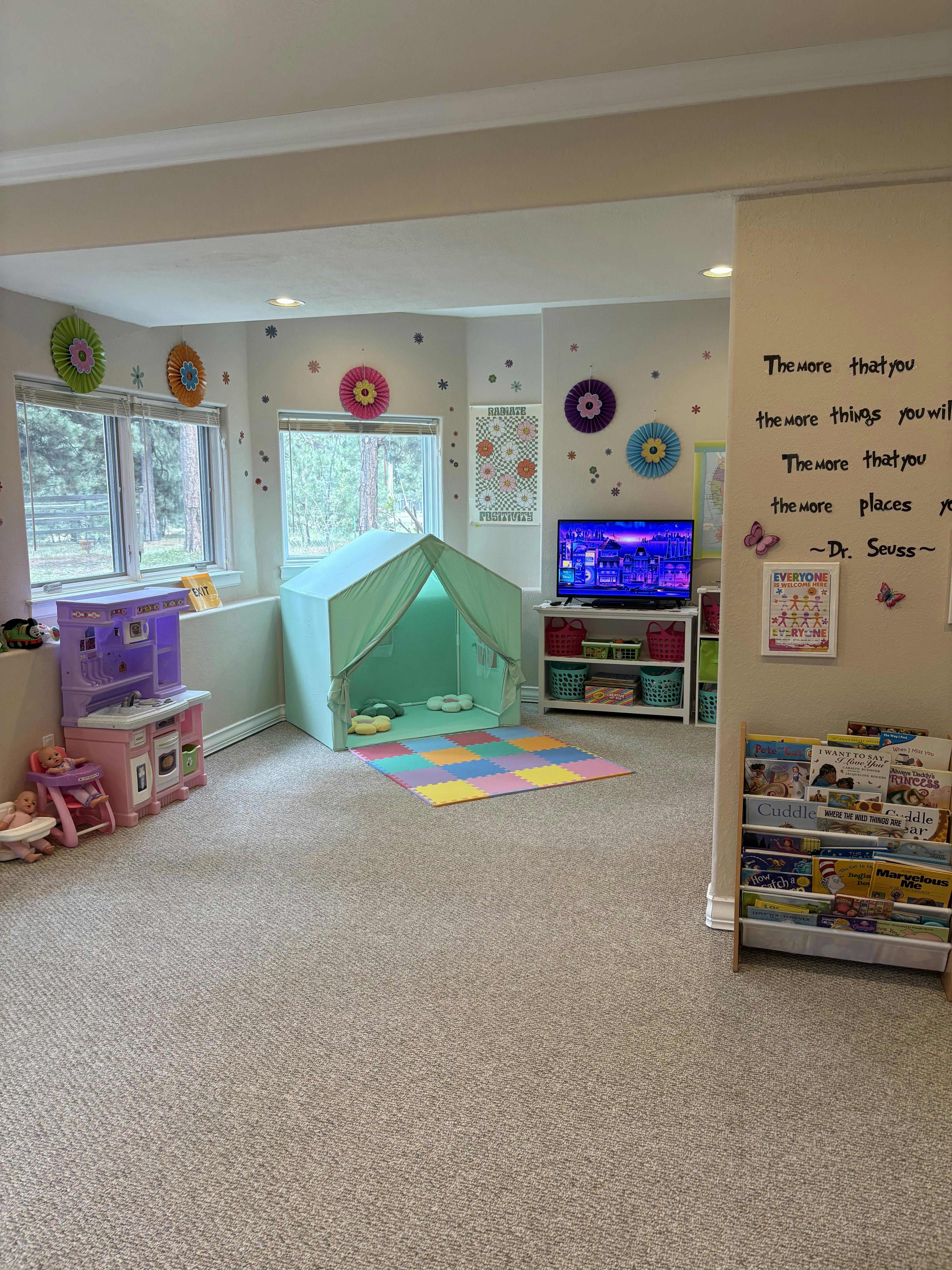 Playroom with a small tent, toy kitchen, bookshelves, and television