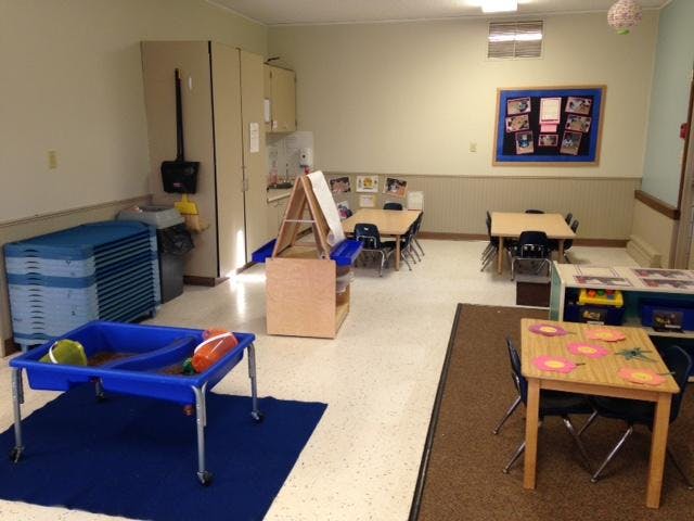 Empty classroom with small tables and chairs, napping cots, and a sand table