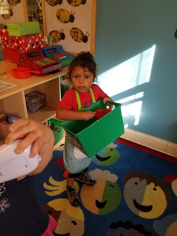 Child holding a green basket in a classroom