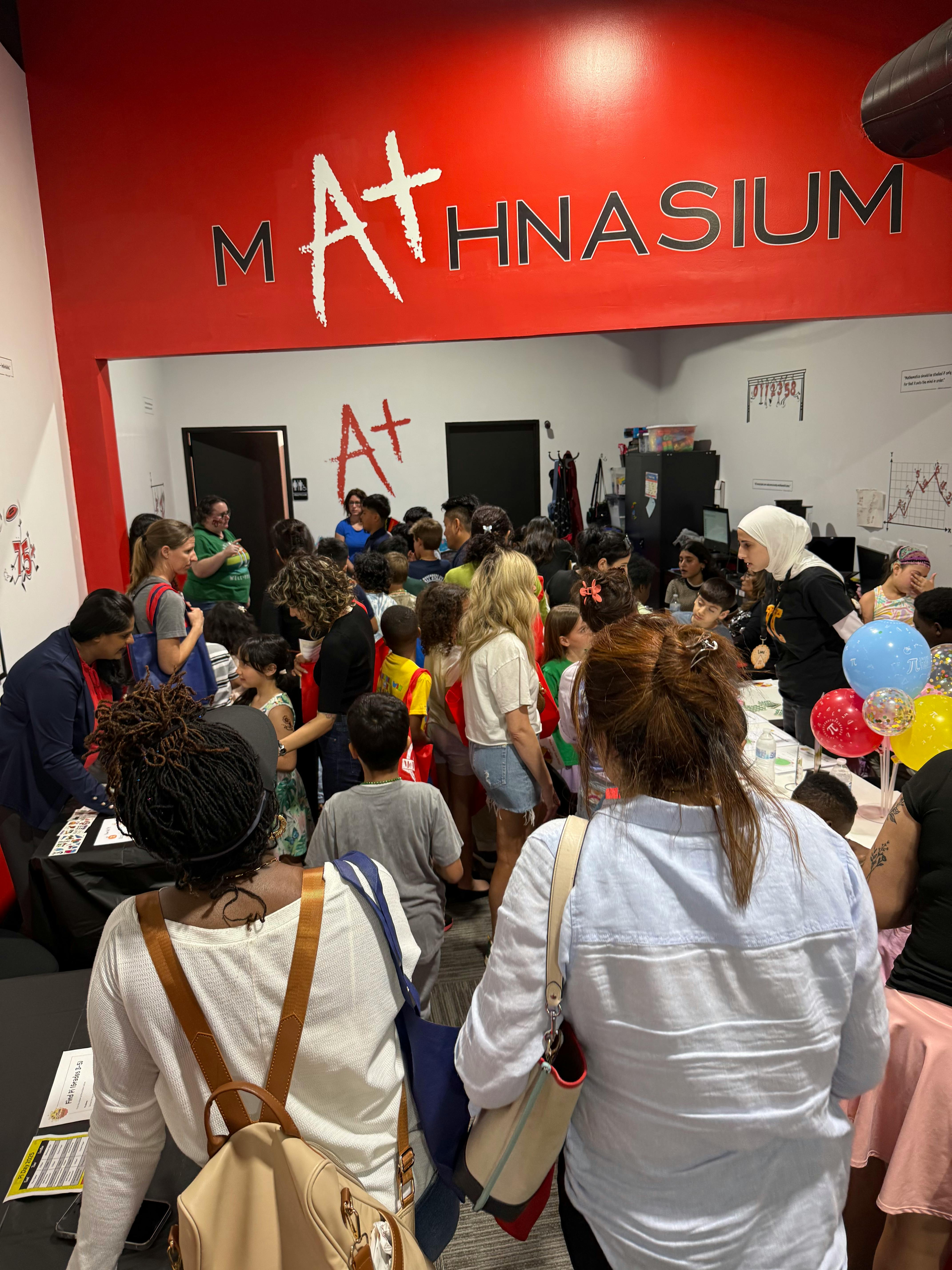 Crowd of people and children in a room with a Mathnasium sign