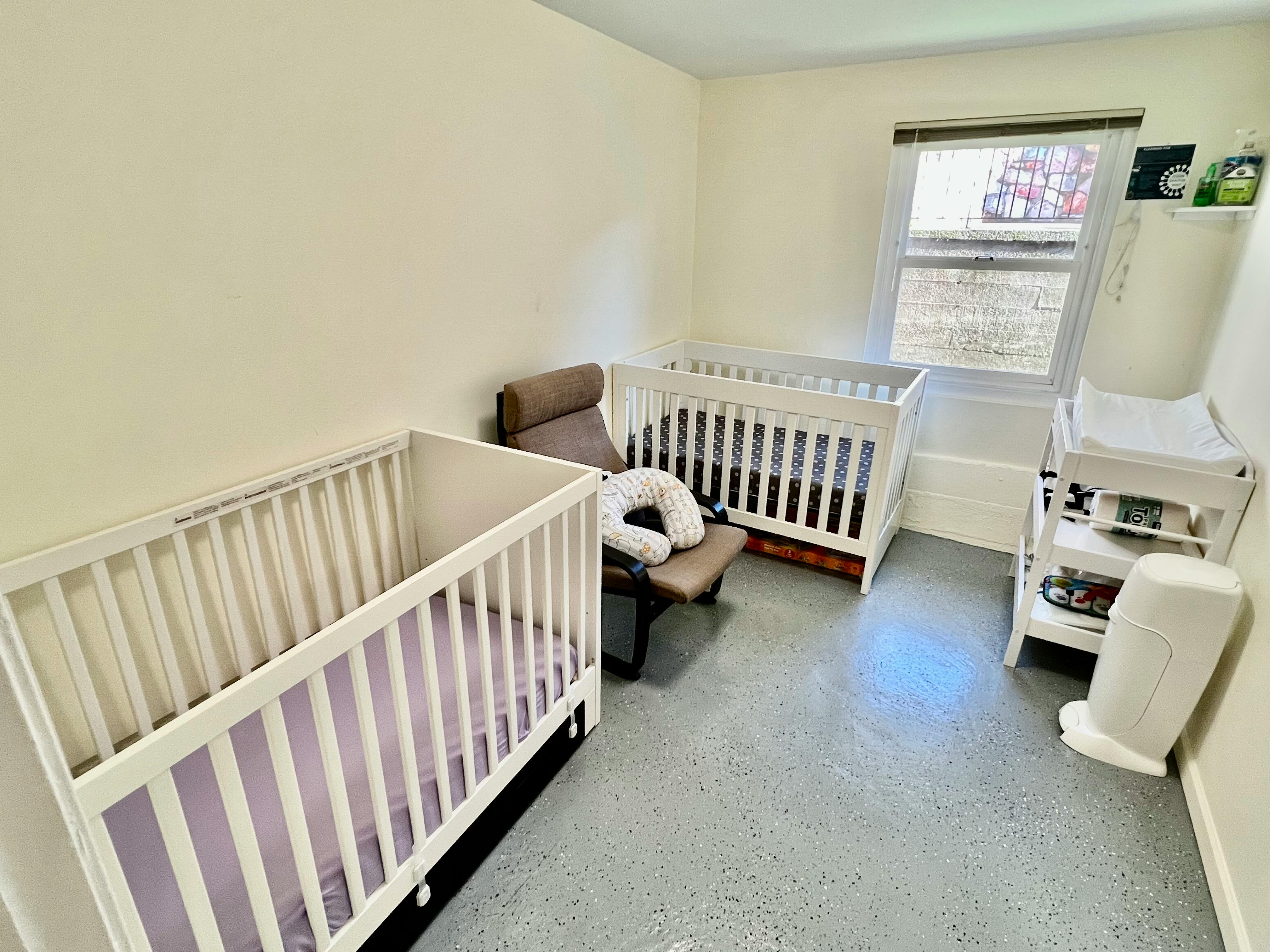Two cribs in a room with a chair and changing table