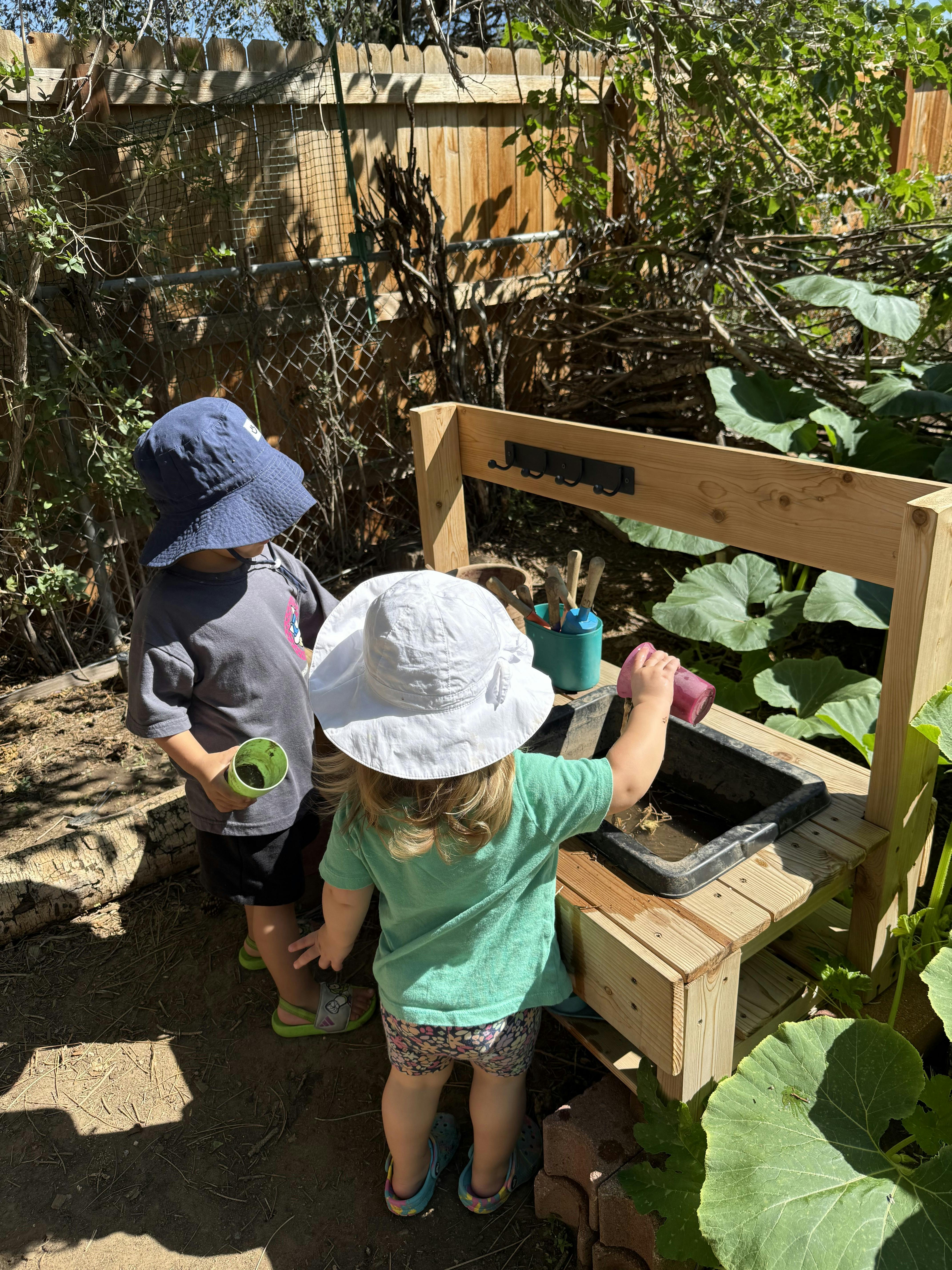 Two children playing with water and toys at a wooden outdoor sensory table