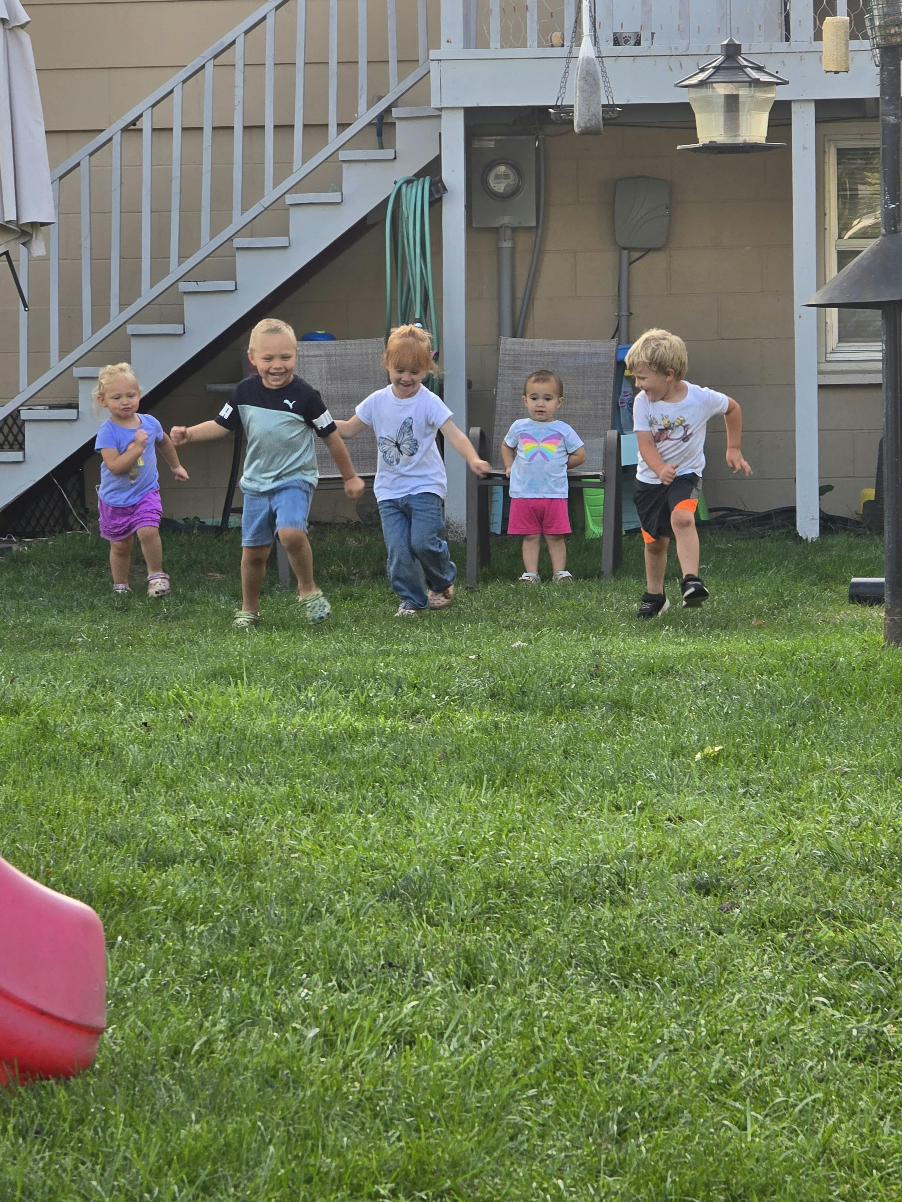 Five children playing in a grassy backyard