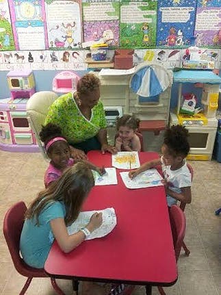 Adult and children drawing at a red table in a classroom