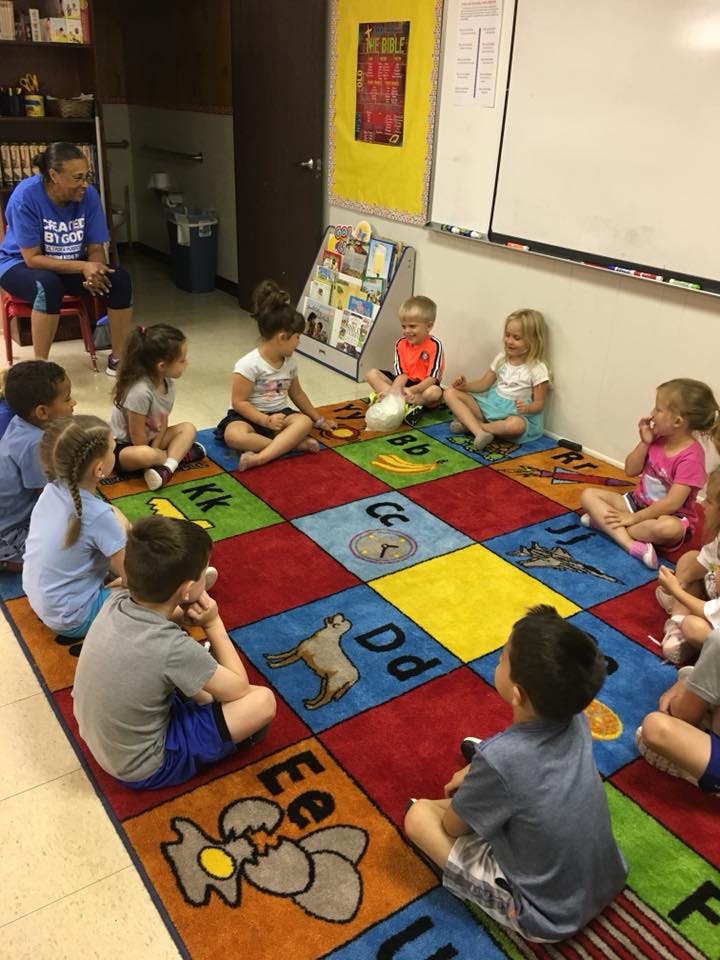 Adult and children sitting on a colorful alphabet rug in a classroom