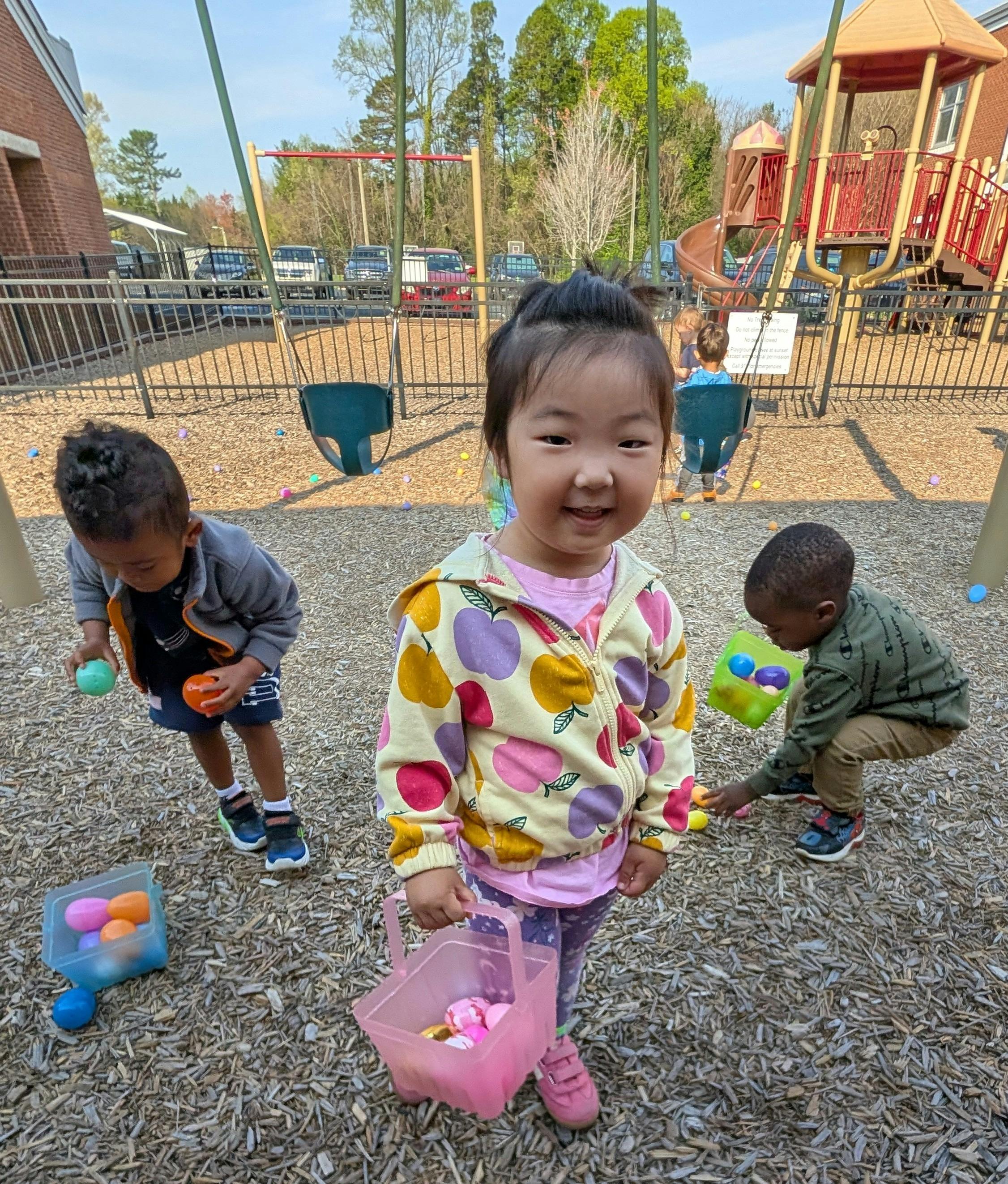 Child holding a basket on a playground with other children collecting eggs