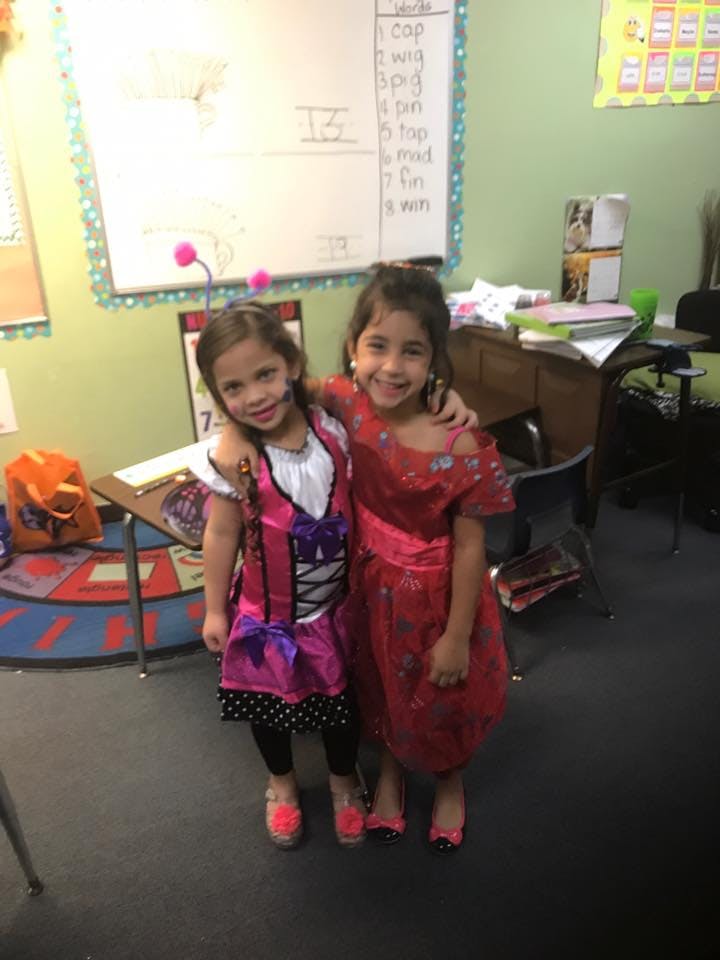 Two children in costumes standing with arms around each other in a classroom