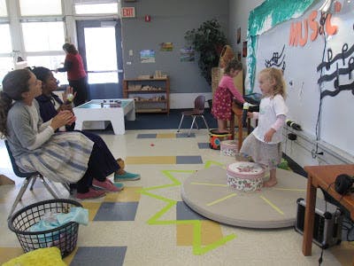 Two children playing with drums in a classroom, two people watching