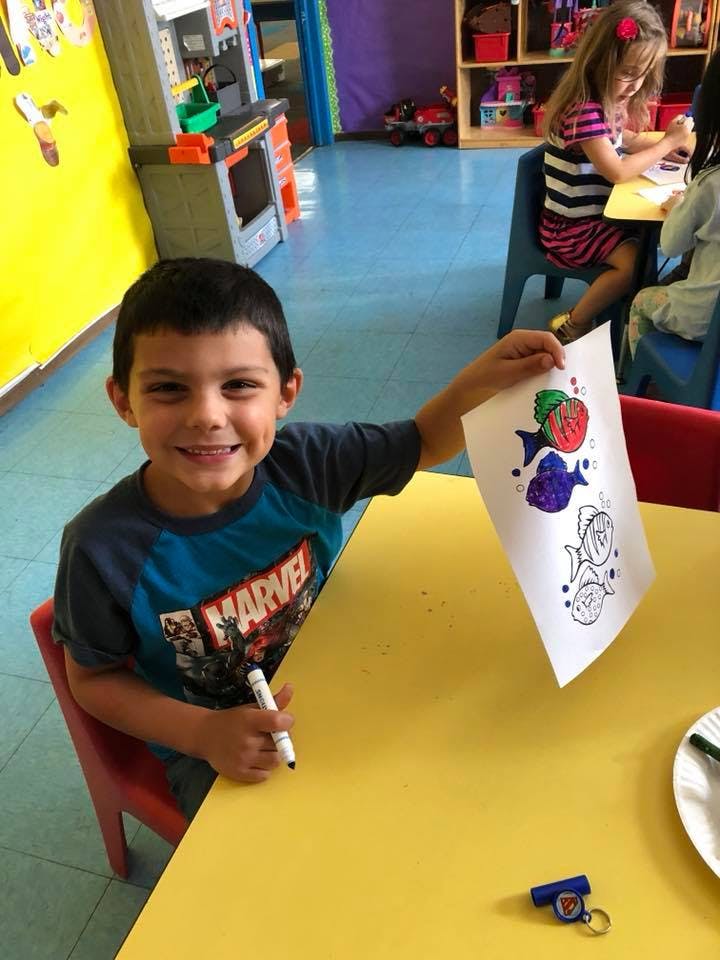 Child holding up a drawing of fish in a classroom