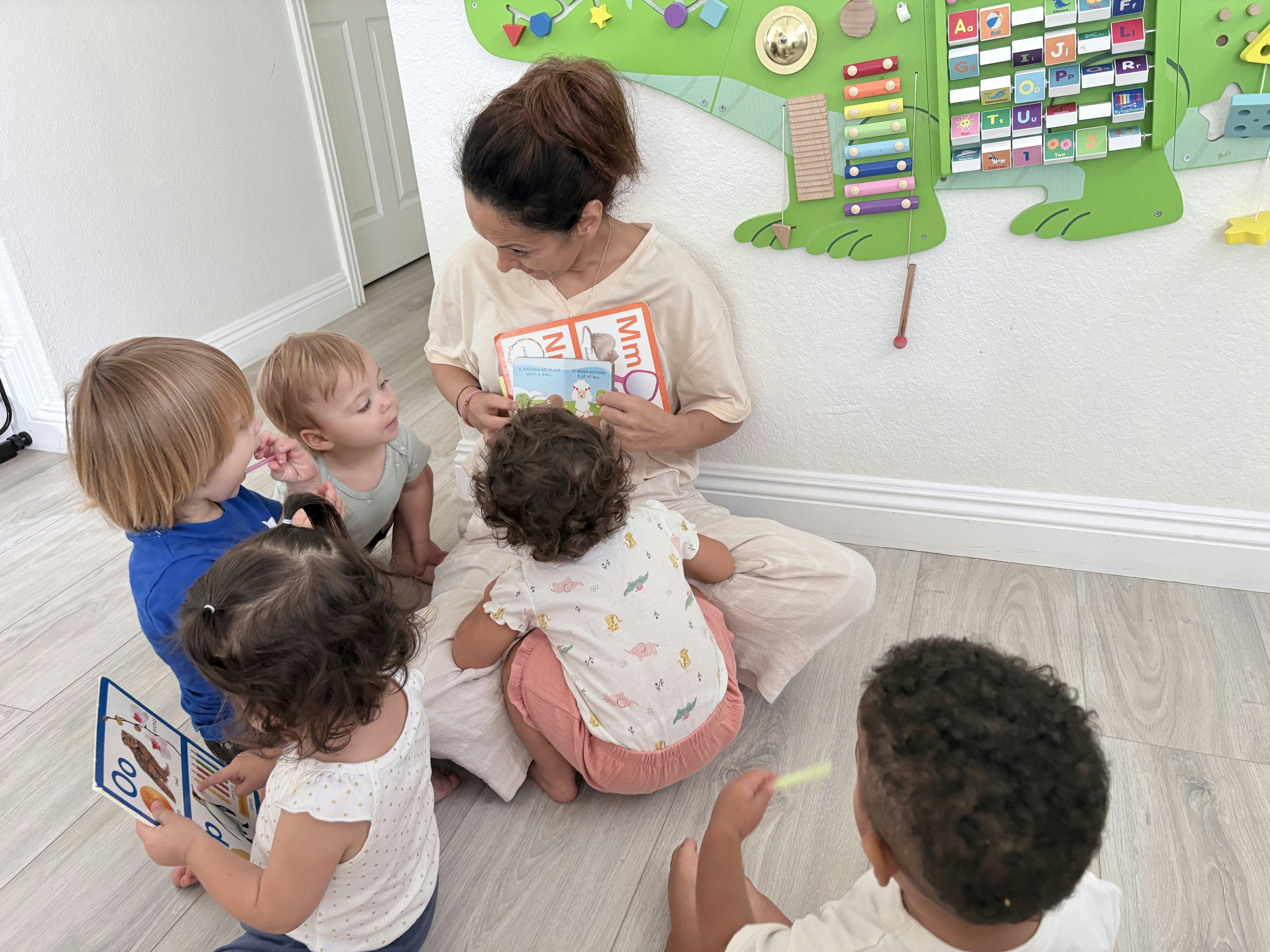 Adult sitting on the floor reading a book to a group of children