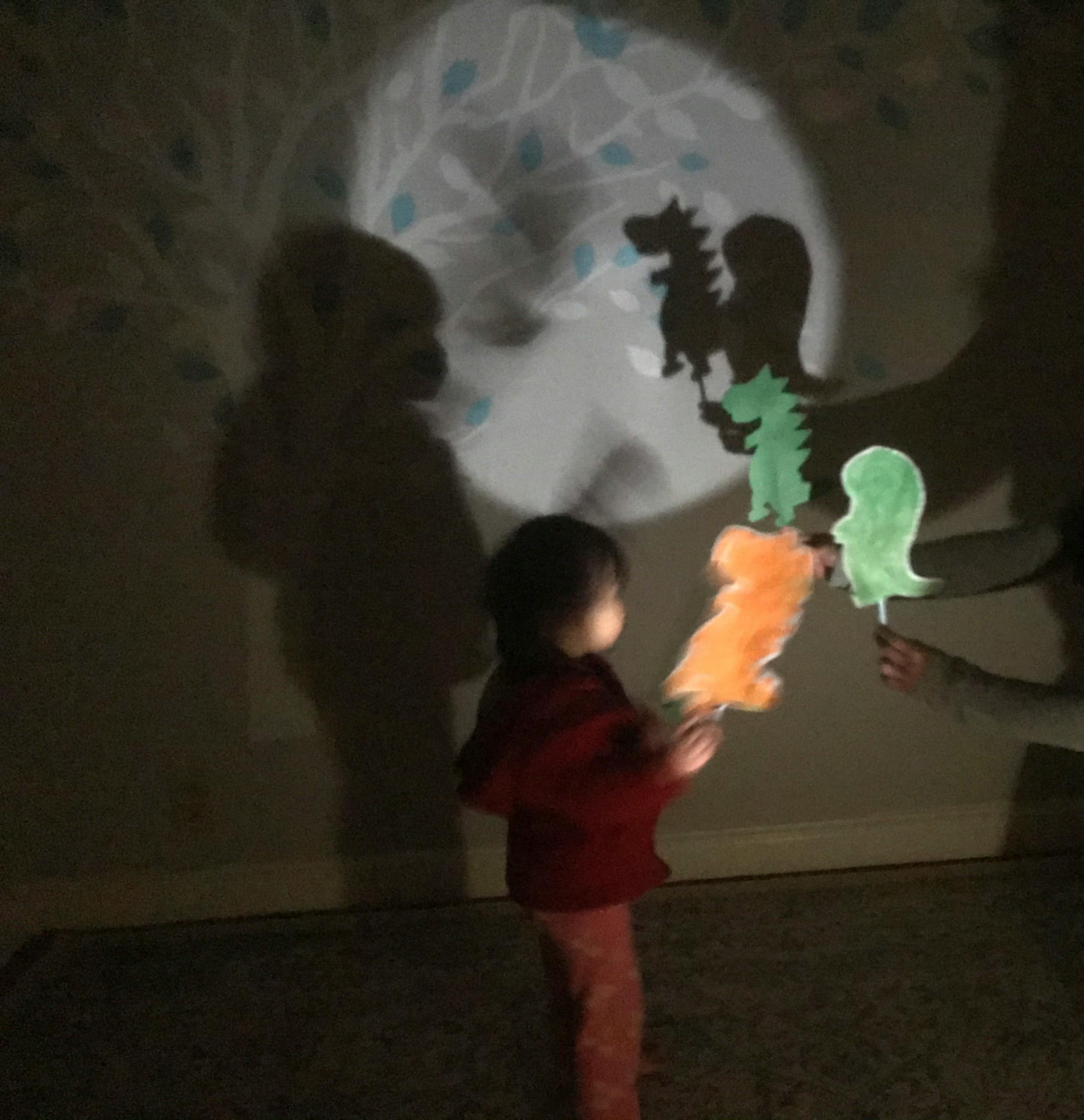Child playing with dinosaur shadow puppets on a wall